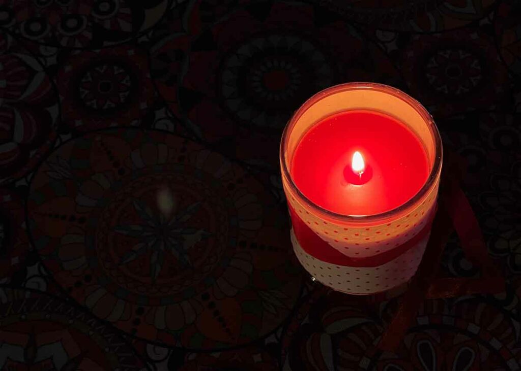 Tända ett ljus. Bild på rött blockljus i ett mörkt rum. Levande ljus.