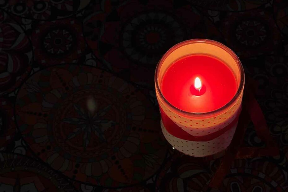 Tända ett ljus. Bild på rött blockljus i ett mörkt rum. Levande ljus.